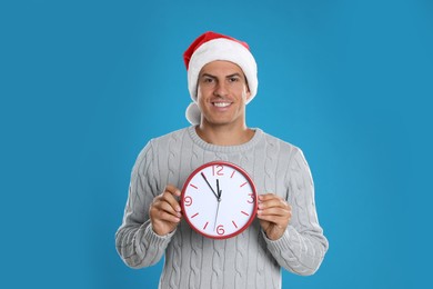 Photo of Man in Santa hat with clock on blue background. New Year countdown