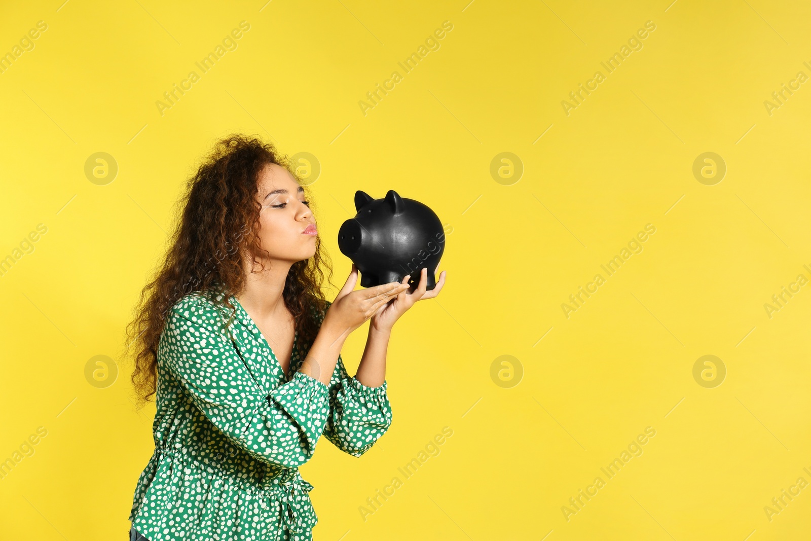 Photo of Young African-American woman with piggy bank on color background, space for text. Money saving