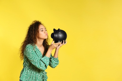 Photo of Young African-American woman with piggy bank on color background, space for text. Money saving