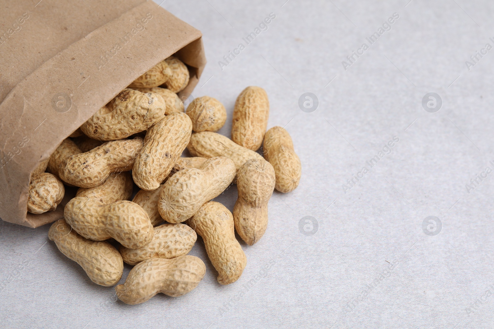 Photo of Paper bag with fresh unpeeled peanuts on grey table, closeup. Space for text