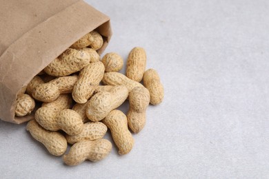 Paper bag with fresh unpeeled peanuts on grey table, closeup. Space for text