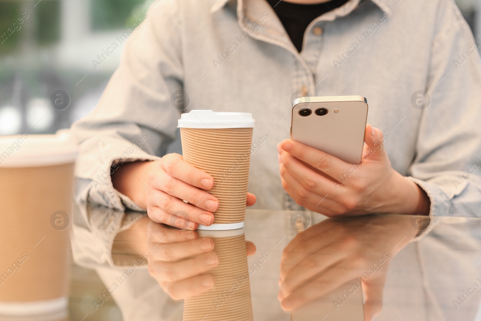 Photo of Woman holding takeaway paper cup and smartphone at table, closeup. Coffee to go