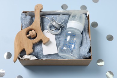 Photo of Different baby accessories with blank card in box and confetti on light blue background