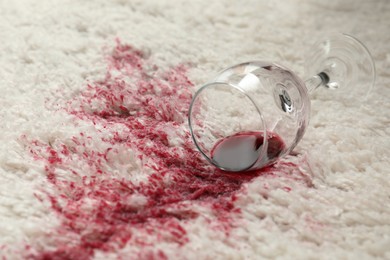 Photo of Overturned glass and spilled red wine on white carpet