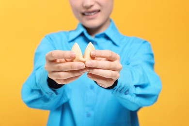 Young woman holding tasty fortune cookie with prediction on yellow background, closeup