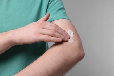 Man applying ointment onto his arm on light grey background, closeup