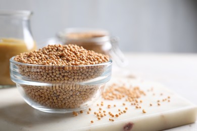 Mustard seeds in glass bowl on board. Space for text