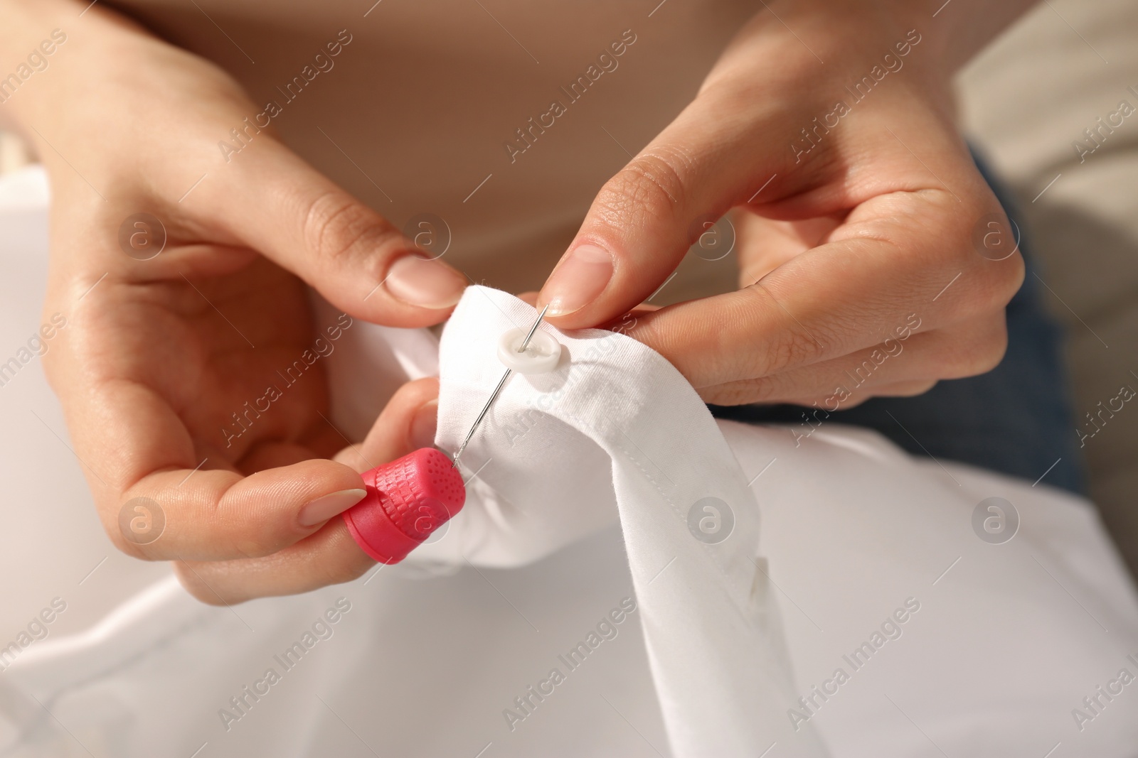 Photo of Woman sewing on white fabric with thimble and needle, closeup