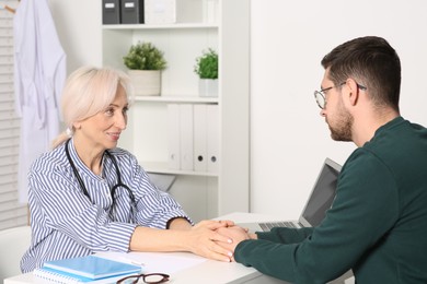 Doctor holding patient's hands at white table during consultation in clinic