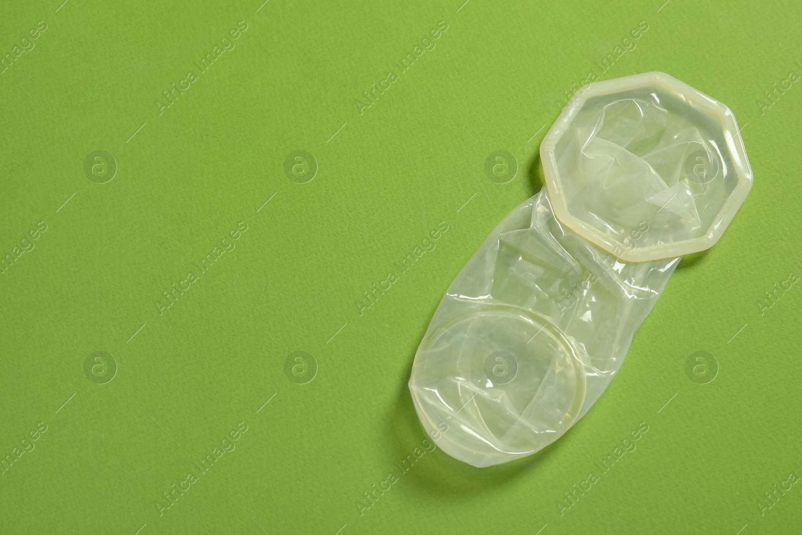 Photo of Unrolled female condom on green background, top view and space for text. Safe sex