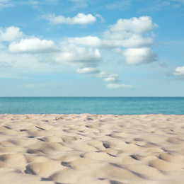 Image of Sandy beach near ocean under blue sky with clouds