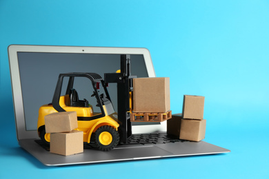 Photo of Laptop, forklift model and carton boxes on light blue background. Courier service