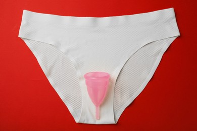 Photo of Menstrual cup and panties on red background, top view