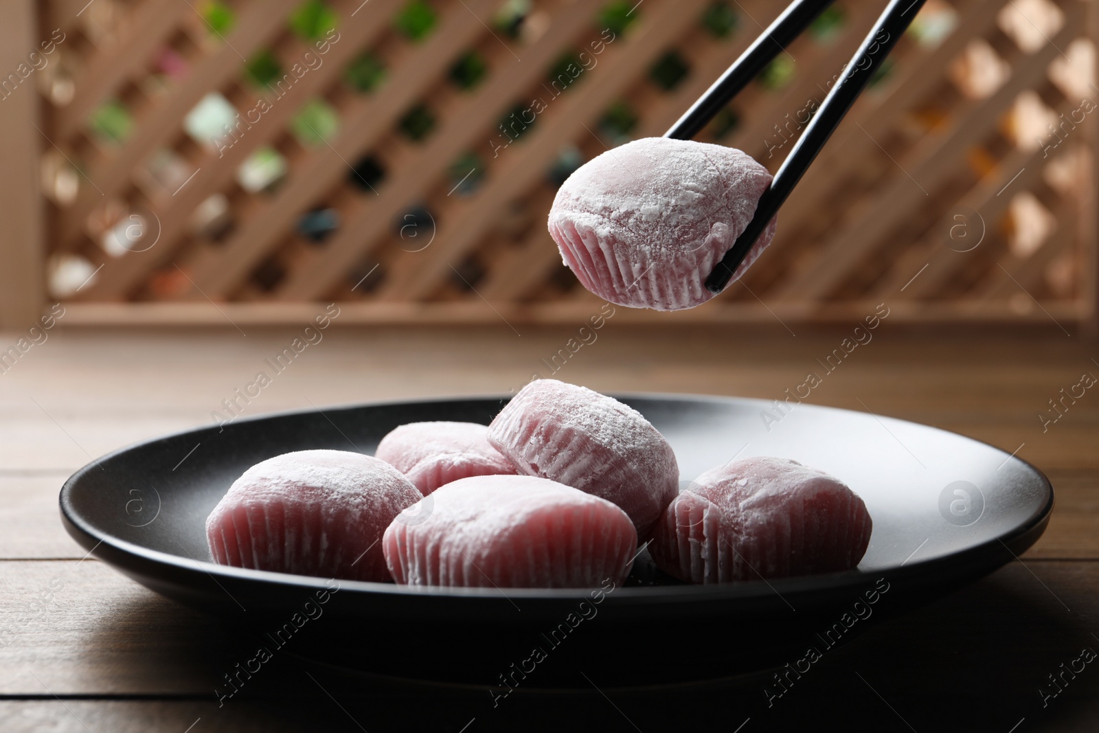 Photo of Taking delicious mochi from plate with chopsticks on wooden table. Traditional Japanese dessert