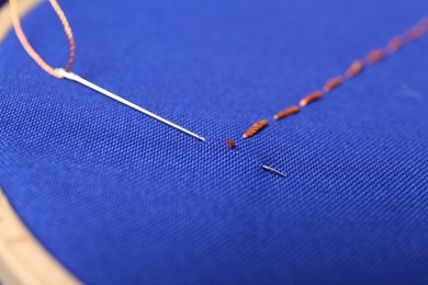 Sewing needle with thread and stitches on blue cloth, closeup