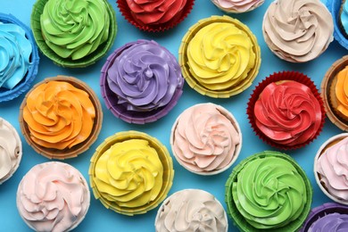 Photo of Many tasty cupcakes with bright cream on light blue background, flat lay