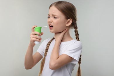 Little girl using throat spray on light grey background