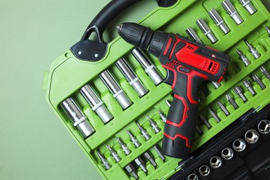 Photo of Electric screwdriver and case with bits on pale green background, top view