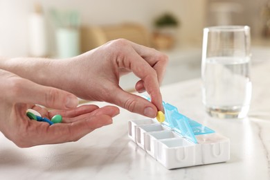 Photo of Woman with pills and organizer at white marble table, closeup