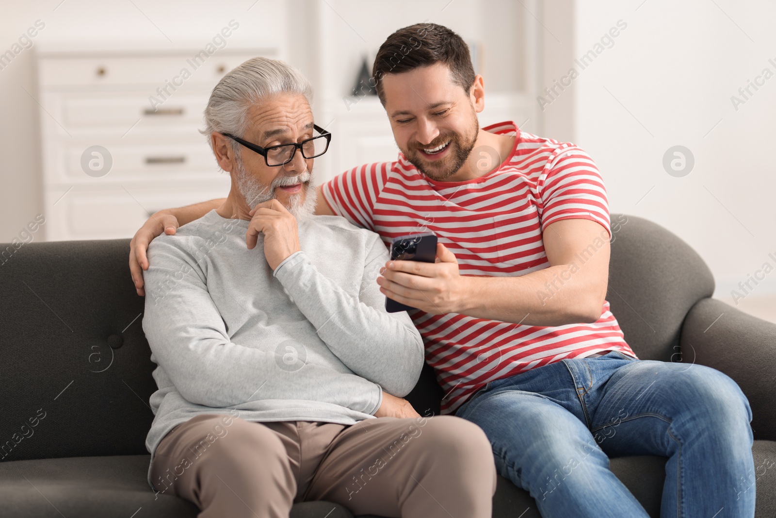 Photo of Happy son and his dad watching something on smartphone at home