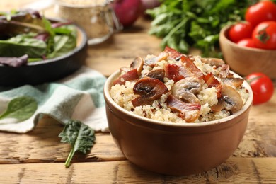 Photo of Tasty quinoa porridge with fried bacon and mushrooms in bowl on wooden table, closeup. Space for text