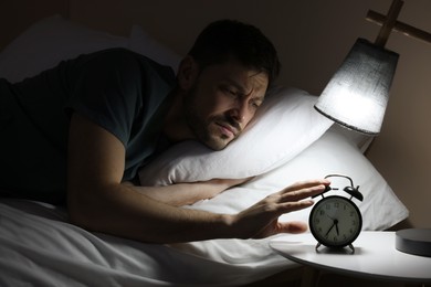 Photo of Sleepy man turning off alarm clock on nightstand in morning