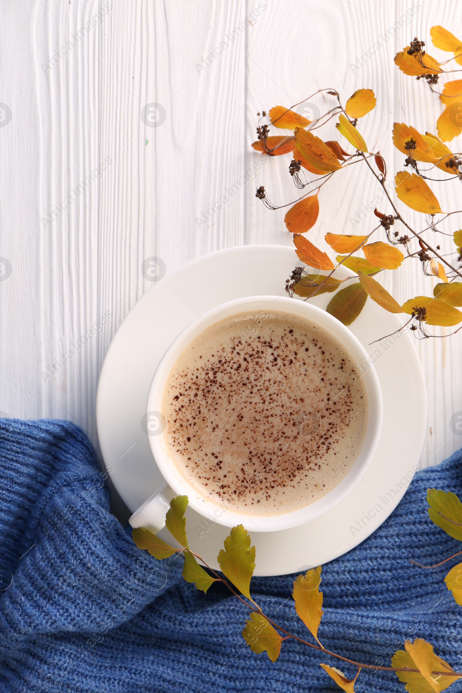 Photo of Cup of hot drink, leaves and knitted sweater on white wooden table, flat lay. Cozy autumn atmosphere