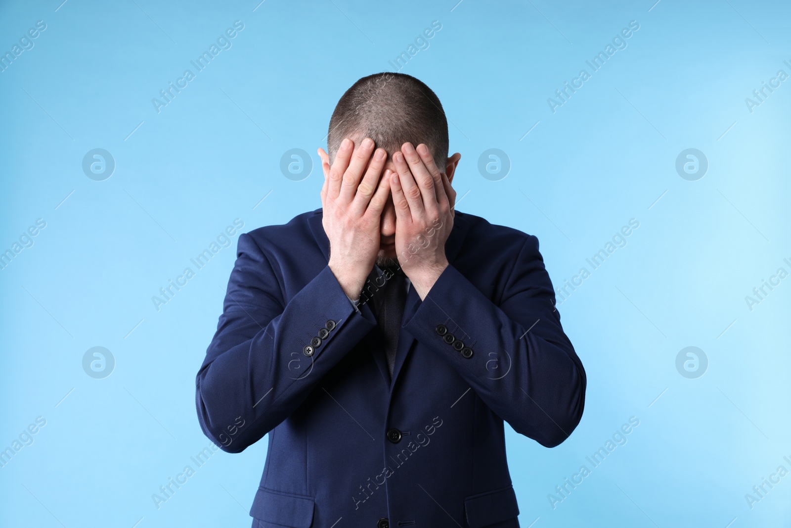 Photo of Upset man in suit closing his face with hands on light blue background