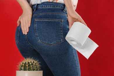 Woman with toilet paper sitting down on cactus against red background, closeup. Hemorrhoid concept