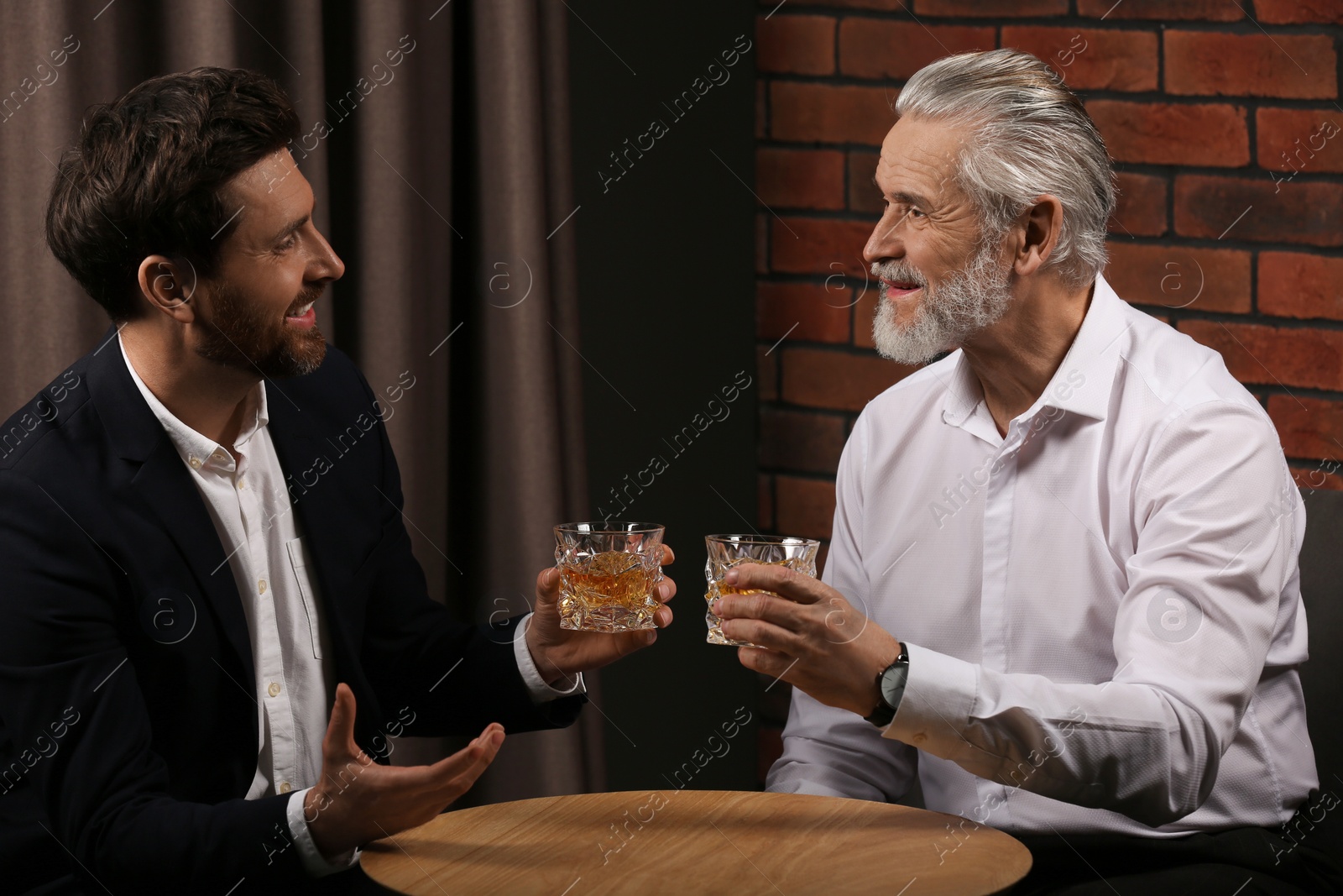 Photo of Men with glasses of whiskey talking at wooden table indoors