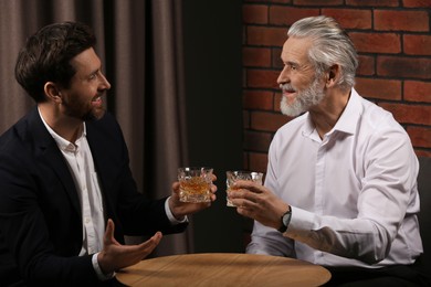 Photo of Men with glasses of whiskey talking at wooden table indoors