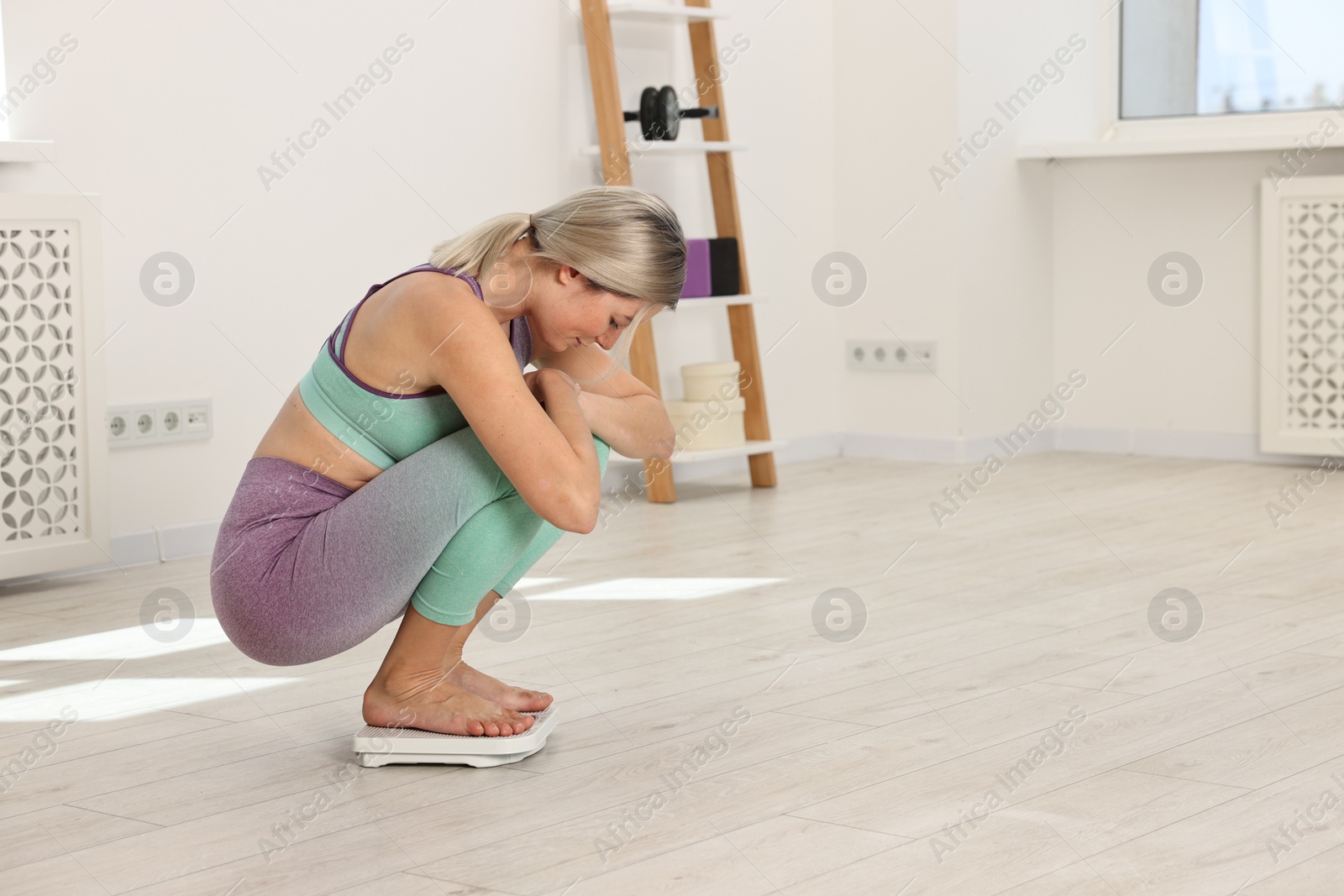 Photo of Woman in sportswear standing on floor scales at home, space for text