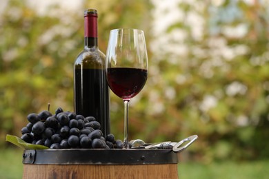 Delicious wine and ripe grapes on wooden barrel outdoors, space for text