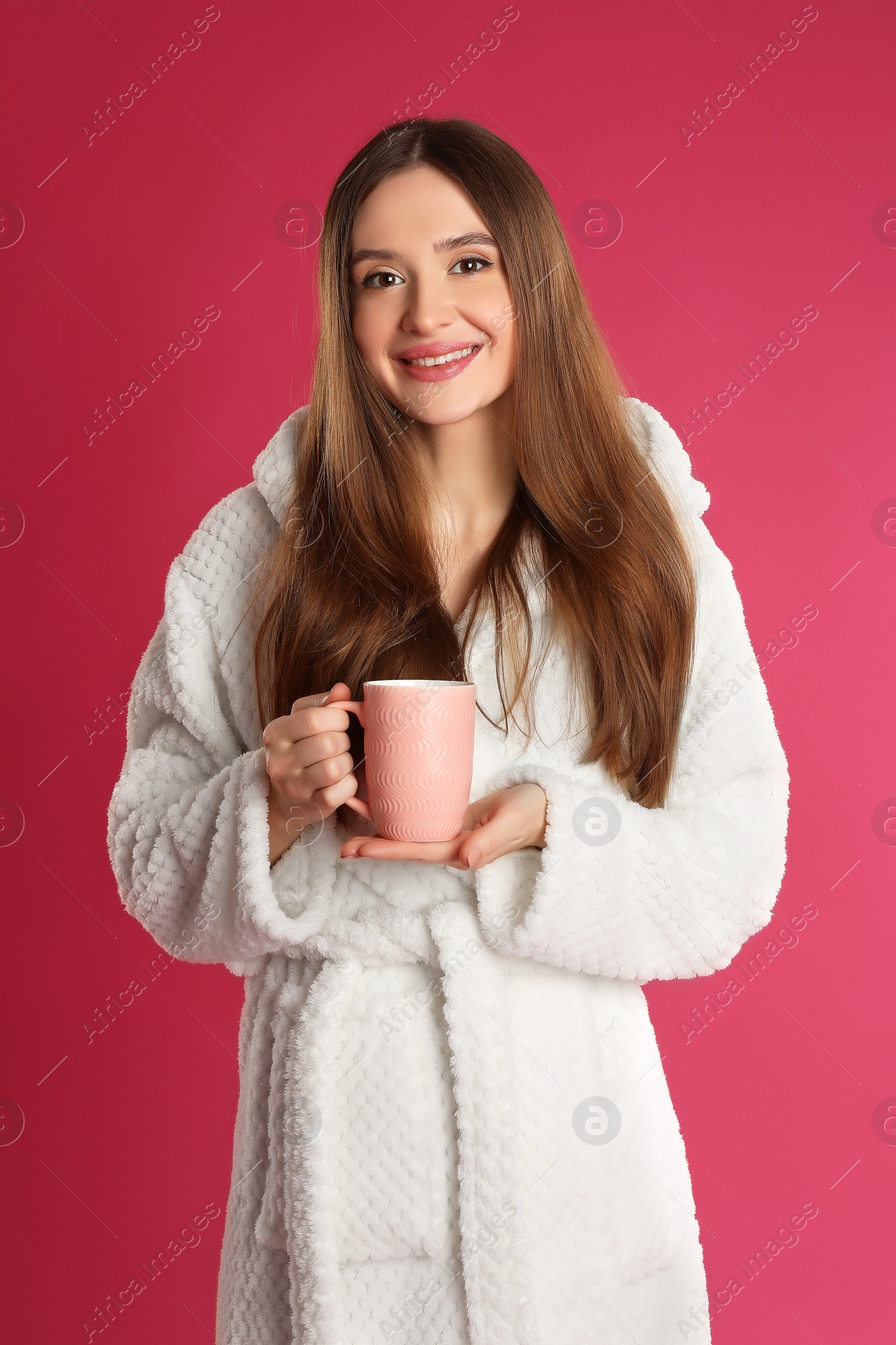 Photo of Young woman in bathrobe with cup of coffee on crimson background