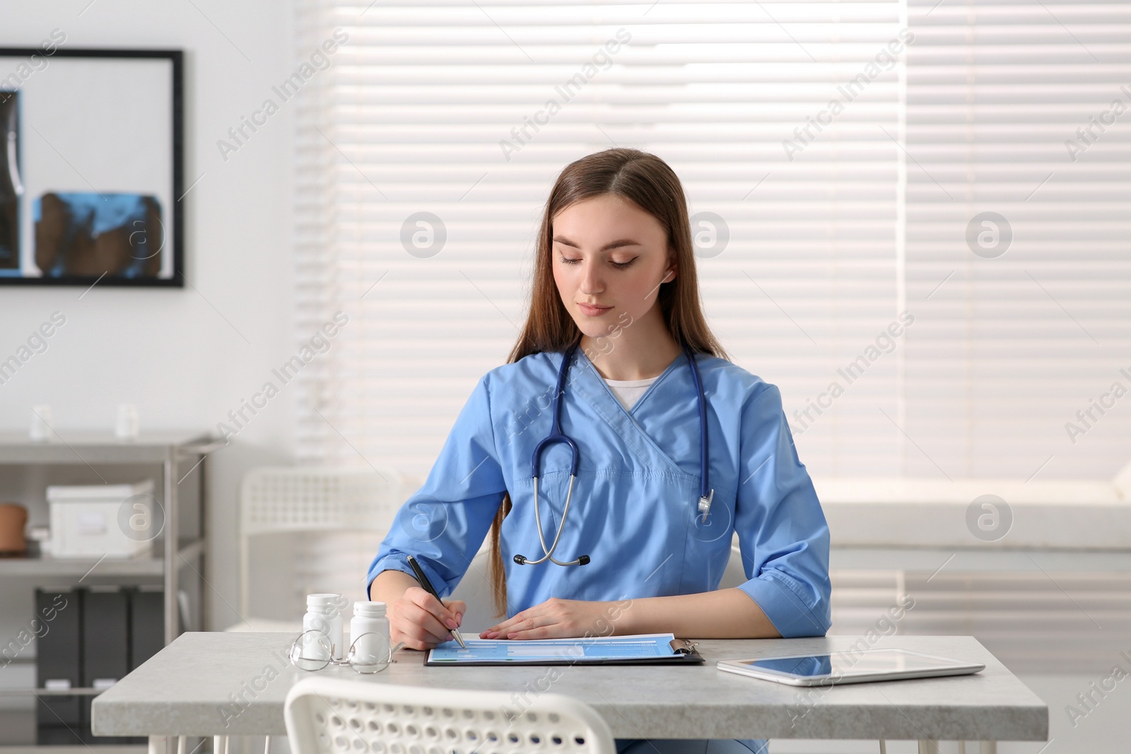 Photo of Doctor filling patient's medical card at table in clinic