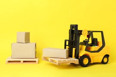 Photo of Toy forklift, wooden pallets and boxes on yellow background