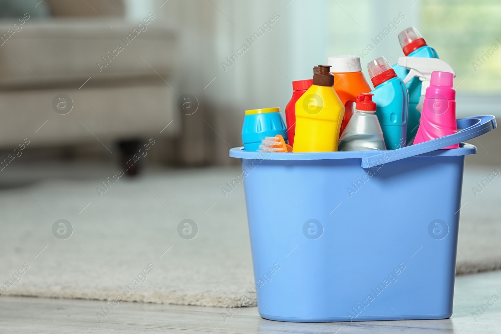 Photo of Plastic bucket with different cleaning products on floor indoors, space for text