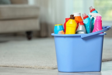Plastic bucket with different cleaning products on floor indoors, space for text