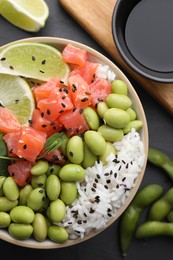 Photo of Delicious poke bowl with lime, fish and edamame beans on black table, flat lay