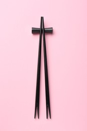 Pair of black chopsticks with rest on pink background, top view