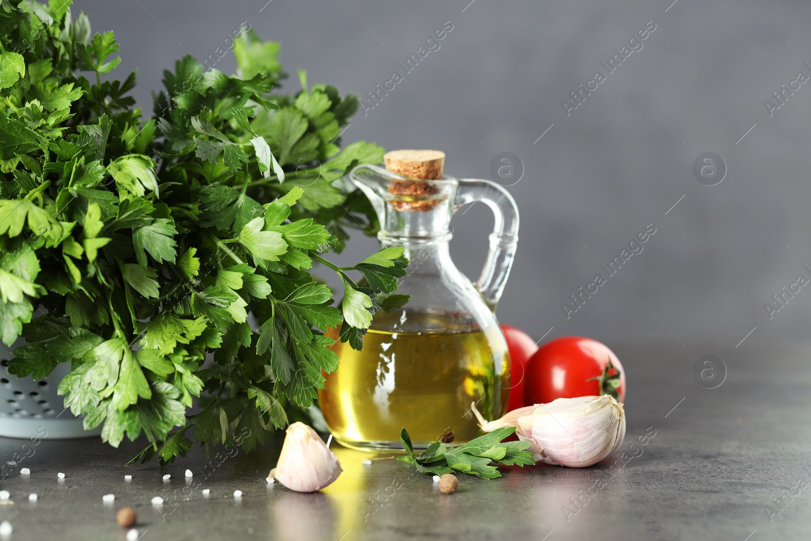 Photo of Fresh parsley, oil and other products on grey table, closeup. Space for text