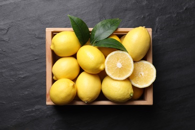 Many fresh ripe lemons with green leaves on black table, top view
