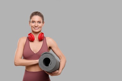 Sportswoman with headphones and fitness mat on grey background, space for text