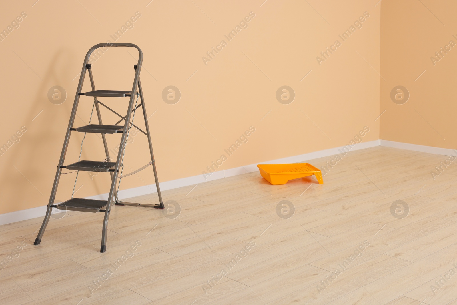 Photo of Metal stepladder near pale orange wall indoors. Room renovation