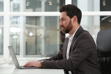 Photo of Man working on laptop at white desk in office