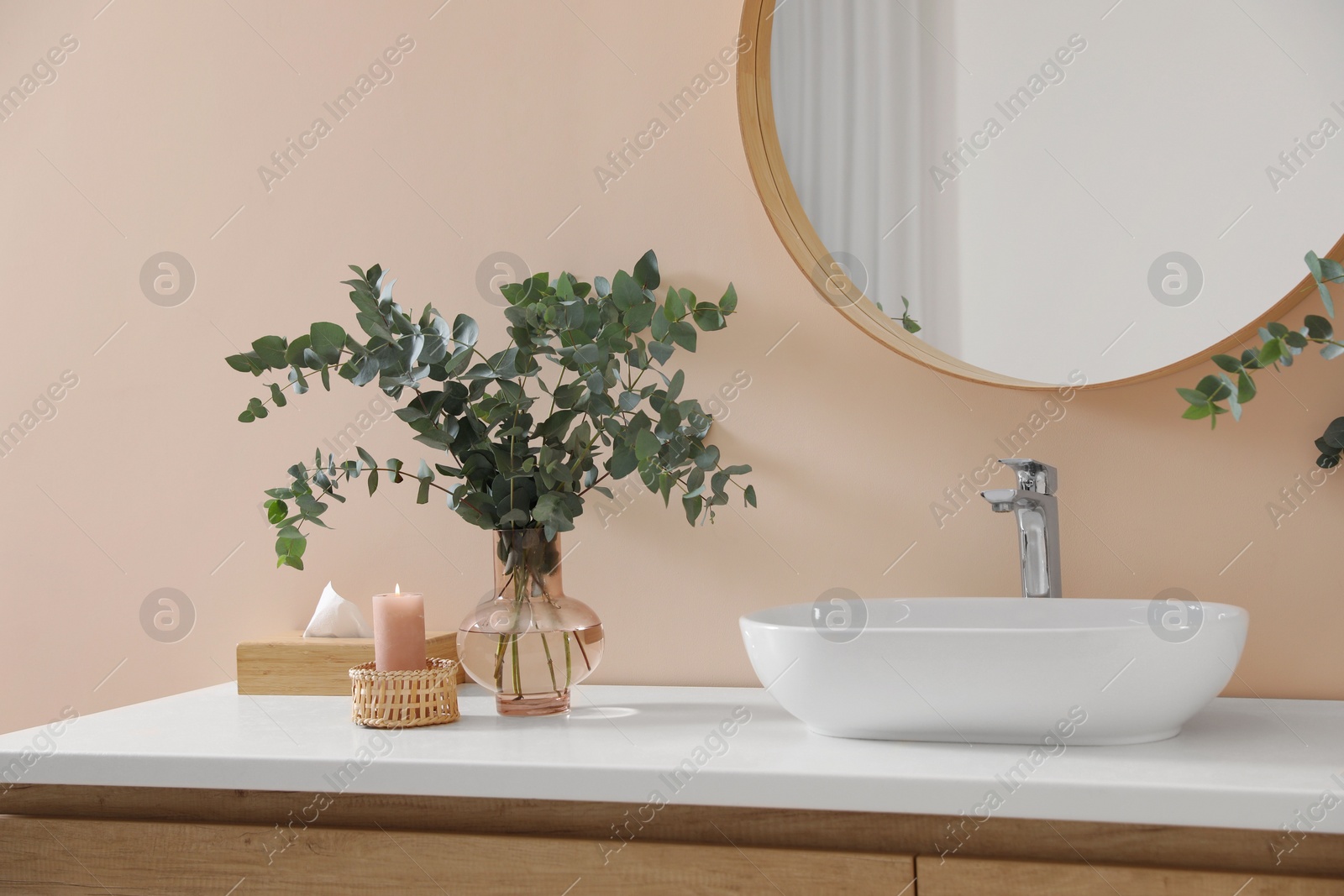 Photo of Eucalyptus branches near vessel sink on bathroom vanity. Interior design