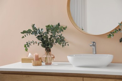 Photo of Eucalyptus branches near vessel sink on bathroom vanity. Interior design