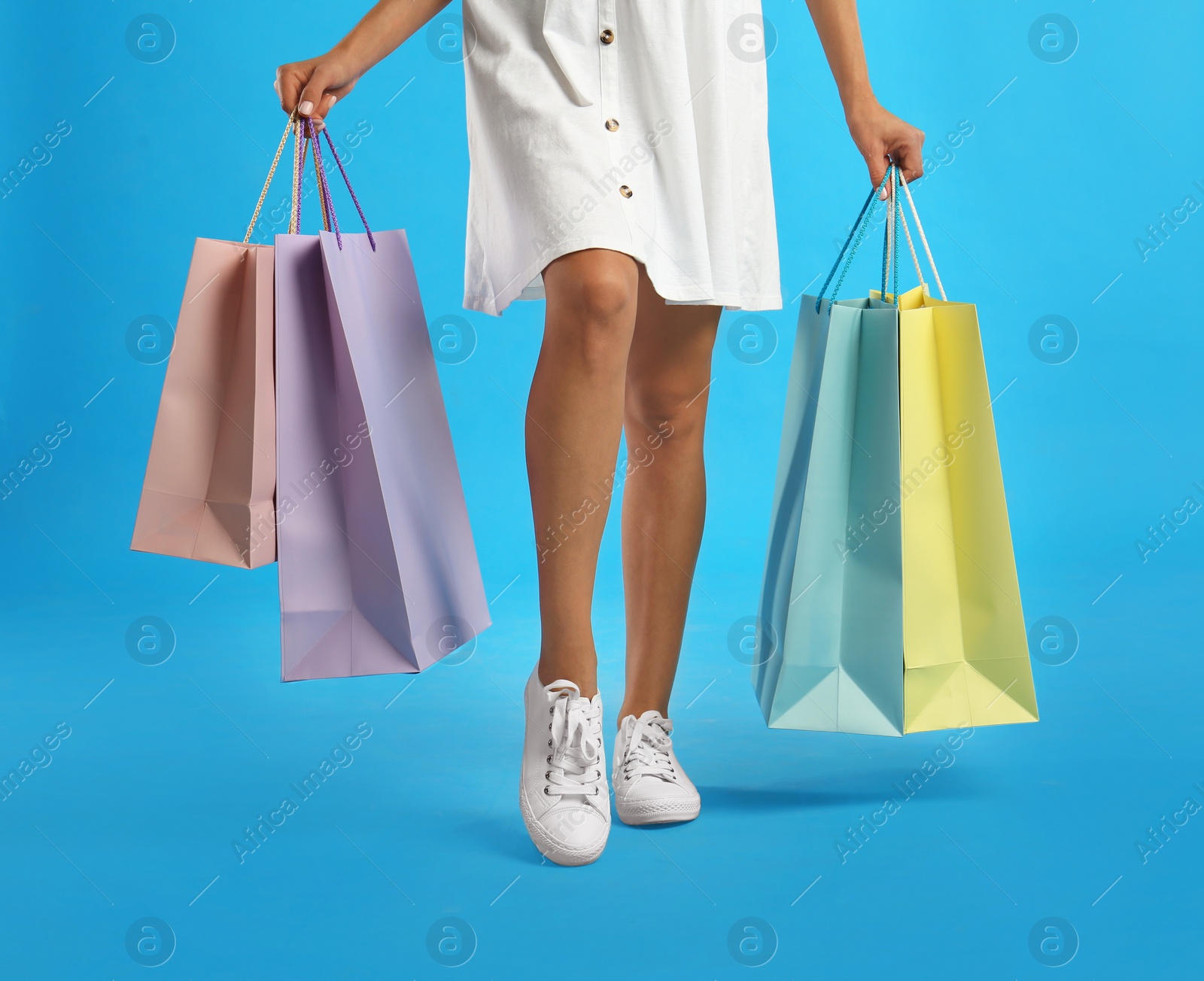 Photo of Young woman with paper shopping bags on light blue background, closeup