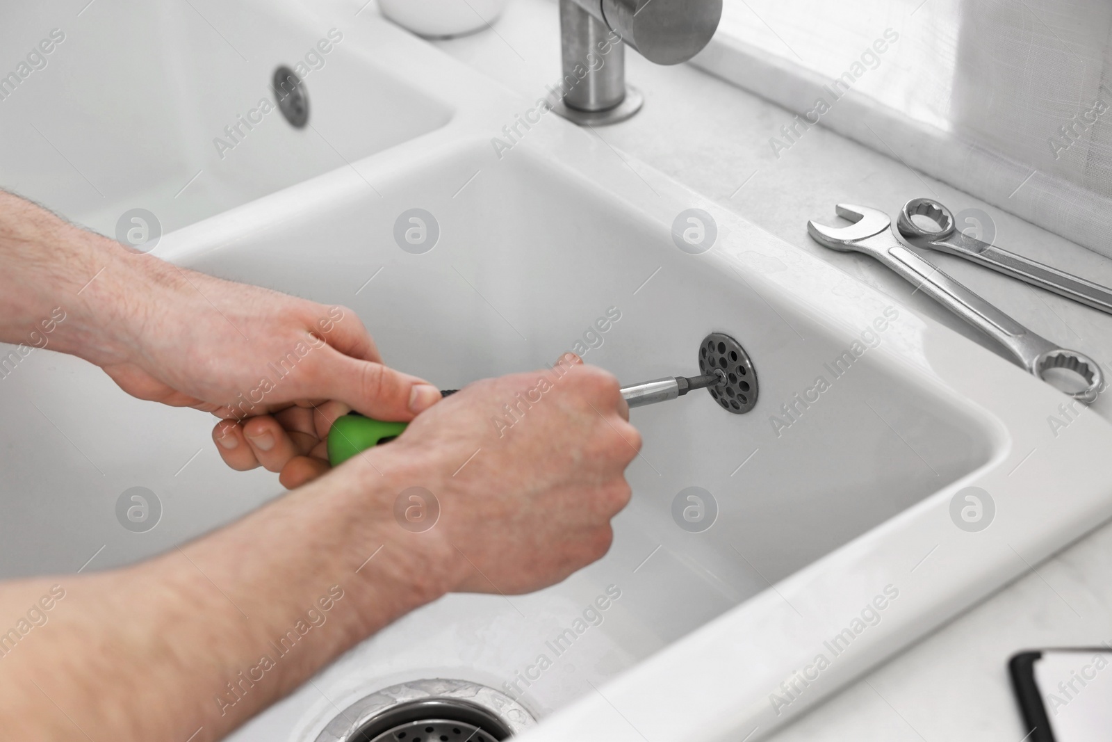 Photo of Plumber repairing sink with screwdriver indoors, closeup
