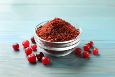 Photo of Cranberry powder in bowl and fresh berries on light blue wooden table, closeup